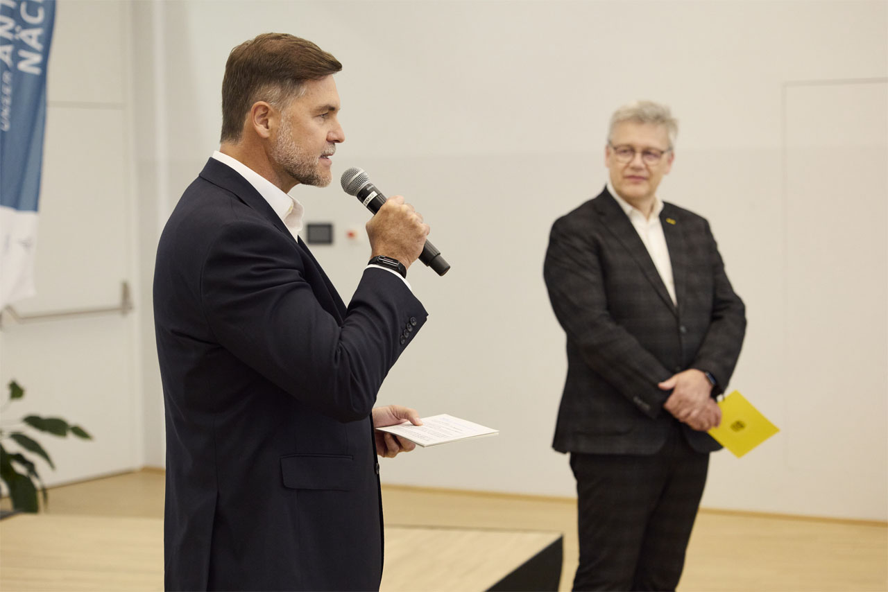 Ein Mann in einem Anzug und einer Krawatte spricht in ein Mikrofon.