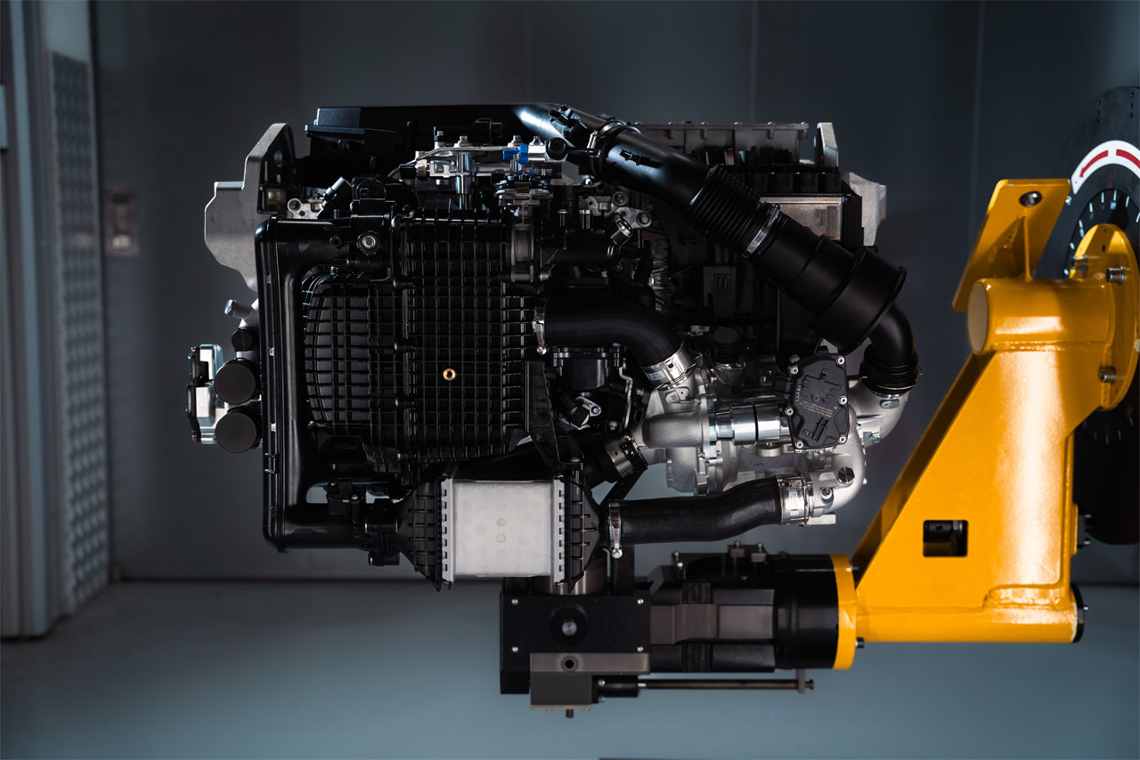 Side view of a complex engine with black and silver components mounted on a yellow support.