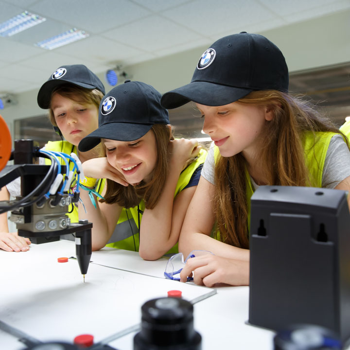Three schoolgirls wearing BMW caps watch a robot during a day in production.
