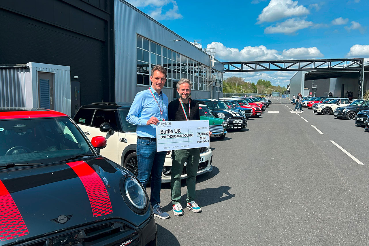 Two men holing up a sign standing next to a black and red MINI cooper
