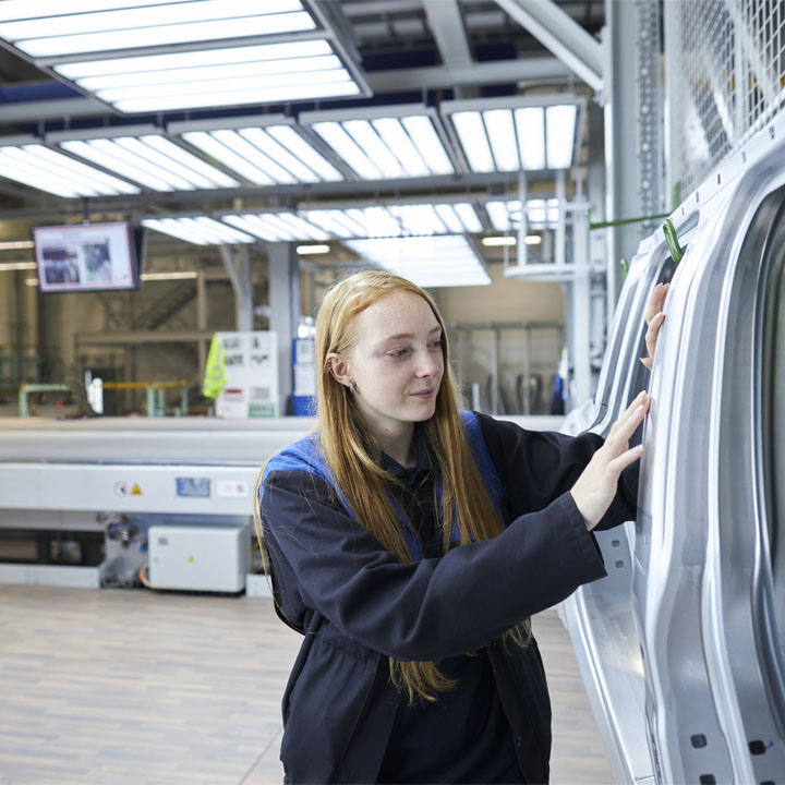  In a factory setting, a woman examines a sturdy metal door, highlighting her focus on the industrial environment.