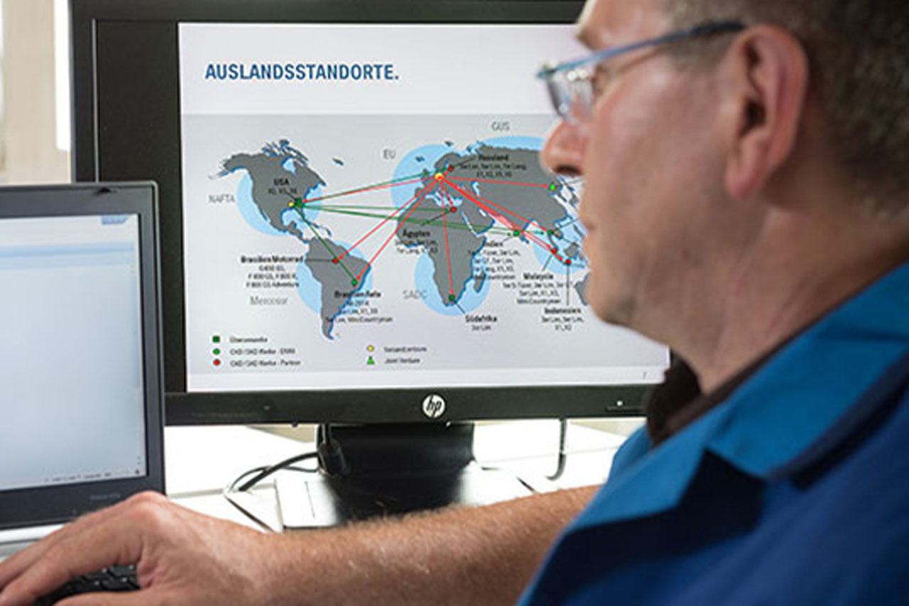 Ein BMW Group Mitarbeiter arbeitet am Computer, auf einem seiner Bildschirme ist eine Weltkarte mit BMW Group Standorten zu sehen.
