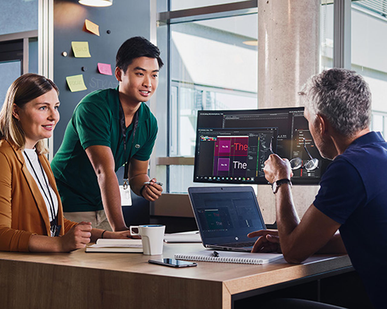 Studierende besprechen ein Projekt zusammen mit einem erfahrenen Mitarbeiter an einem Bildschirm im Büro.