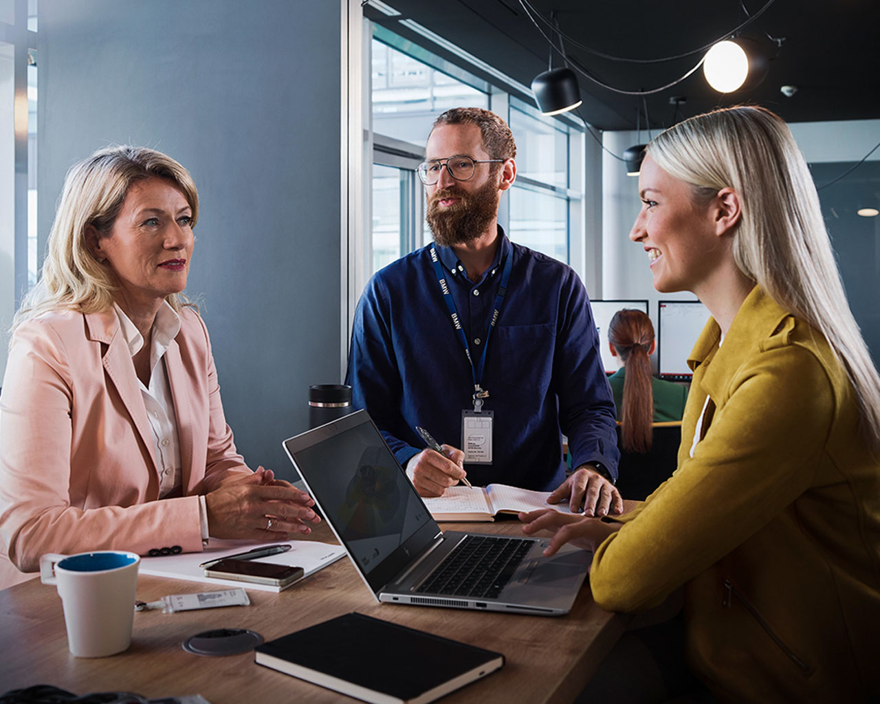 Zwei Berufserfahrene Mitarbeiter bei der BMW Group unterhalten sich in moderner Büroumgebung.