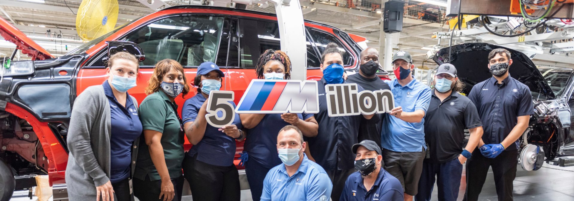 Five Millionth Vehicle, BMW X5 M Competition, on assembly line with associates in front of it holding a graphic sign. 